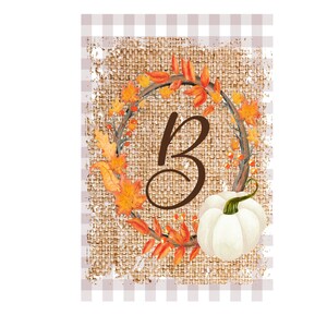 Op de afbeelding: Een herfstontwerp met de bruine letter "B" omcirkeld door een krans van oranje en gele herfstbladeren en bessen. Een witte pompoen staat onder de letter. De achtergrond heeft een jute textuur met een lichtbruin en wit geblokt patroon.