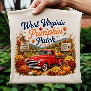 Può includere: Un articolo in tessuto color crema con la grafica di un pickup rosso vintage in un campo di zucche. Il testo recita West Virginia Pumpkin Patch, Fresh Pumpkins Hayrides Apple Cider e Almost Heaven West Virginia con paesaggio montano.