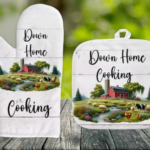 May include: A set of two white cotton kitchen pot holders with a farmhouse theme. The pot holders feature a red barn, green trees, a stream, and sheep. The text "Down Home Cooking" is printed on both pot holders.