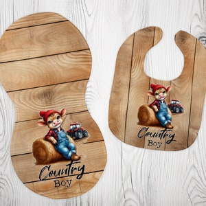 May include: A brown wooden baby bib and burp cloth with a cartoon illustration of a cow wearing overalls and a red hat sitting on a bale of hay. The text "Country Boy" is printed on both items.