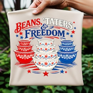 以下が含まれることがあります： ベージュのトートバッグ。赤と青で「Beans, 'Taters & Freedom」の文字。赤い、白、青のミキシングボウルと花柄、星のイラストが描かれています。