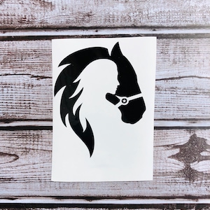 May include: A black vinyl decal featuring a silhouette of a horse head with a flowing mane. Within the negative space of the horse's neck and mane, the profile of a person is visible. The horse wears a halter with a small star detail.