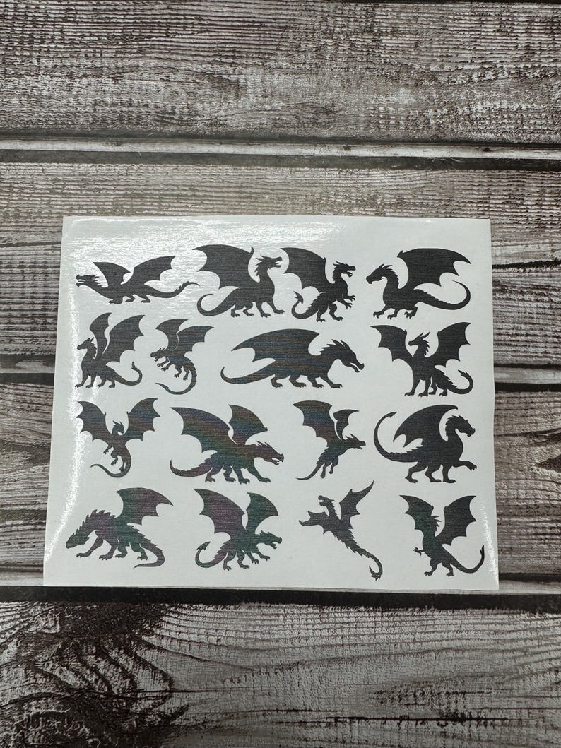 May include: A white rectangular sheet featuring a collection of fifteen individual black dragon silhouettes in various poses, including flying, standing, and crouching positions, arranged in a grid pattern across the surface.
