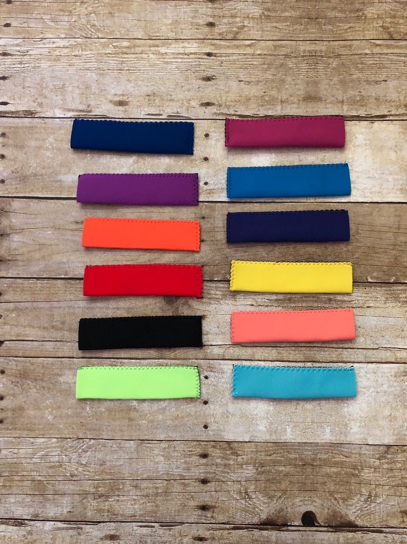 May include: A collection of colorful, rectangular neoprene drink sleeves in various shades, including blue, purple, orange, red, black, green, yellow, and pink. Each sleeve has a scalloped edge and is designed to insulate beverages.