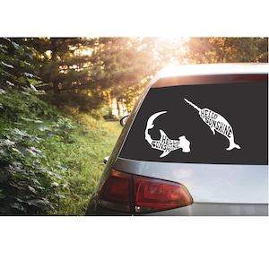 May include: A white car with a black rear window. The rear window has two white decals of a hammerhead shark and a swordfish. The decals are shaped like the animals and the words "Hello Sunshine" are written inside the shapes.