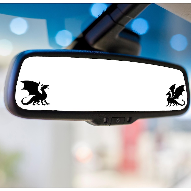 May include: A black rectangular rearview mirror featuring two black dragon silhouettes, one positioned on the far left and one on the far right, facing towards the centre of the mirror surface against a clear, reflective white background.