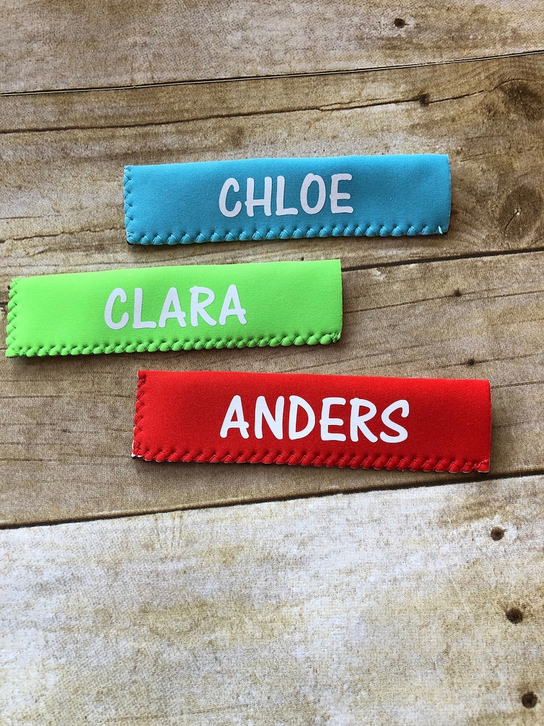 May include: Three rectangular, colorful fabric items with white text spelling out names. The top one is teal and says "CHLOE", the middle one is lime green and says "CLARA", and the bottom one is red and says "ANDERS".