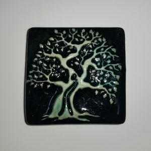 May include: A ceramic tile with a raised, white tree design on a dark green background.