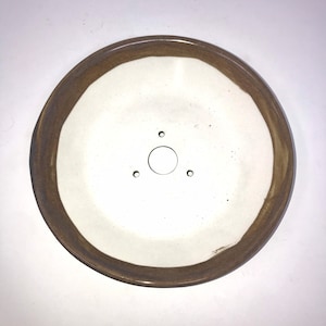 May include: A white ceramic saucer with a brown rim. The saucer has three small holes and a larger hole in the center.