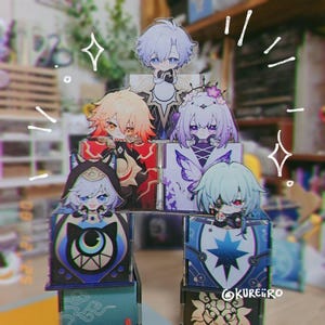 May include: A pyramid of colorful anime-style character figures. Each figure is perched on a decorated box. The characters have unique hair colors and outfits. The boxes feature various designs, including stars and geometric patterns.