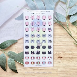 Puede incluir: Una hoja de pegatinas rectangular con una cuadrícula de pequeños emoticonos de personajes. El texto superior dice "GOT DROPPED INTO A FURRY STORY STILL GOTTA EMOTE". La hoja muestra filas de conejos rosas, gatos grises, gatos negros y caras coloridas.