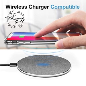 May include: A gray wireless charging pad with a fabric top and a white border. A clear phone case with a phone inside is being placed on the charging pad.