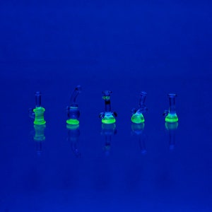 May include: Five small glass bongs in various shapes and sizes, all glowing green under a blacklight.
