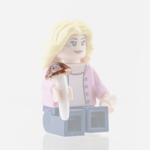 Könnte beinhalten: Eine blonde Lego-Figur in einem rosa Shirt und blauen Jeans hält einen braunen und weißen Pilz.