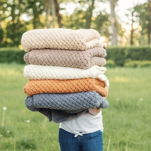 Può includere: Un mucchio di cinque coperte di maglia in vari colori, tra cui beige, marrone, bianco, arancione e grigio. Le coperte sono piegate e impilate l'una sull'altra, con la coperta in basso che è la più grande e la coperta in alto che è la più piccola.