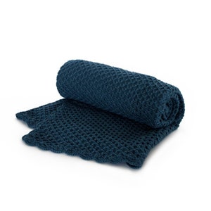 Pode incluir: Uma manta de malha azul escura com uma textura de waffle. A manta est&aacute; enrolada e tem uma borda festoneada.