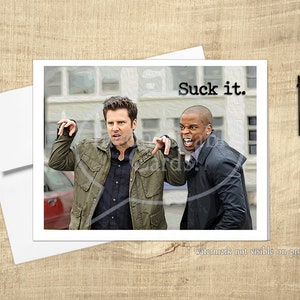 May include: A greeting card featuring a photo of two men, one wearing a green jacket and the other a black jacket, both making a gesture with their hands. The text "Suck it." is printed in black at the top of the card.
