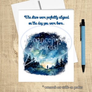 May include: A watercolor illustration of a starry night sky with a single figure standing in a forest. The text "The stars were perfectly aligned on the day you were born." is written above the image.