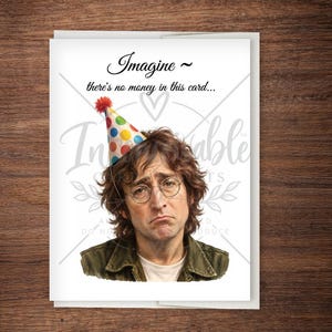 May include: A white greeting card featuring a portrait of a man with brown hair and round glasses wearing a colorful polka-dot party hat. The text above the portrait reads Imagine ~ there's no money in this card... in black script and serif font.