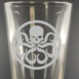 May include: A clear glass pint glass with a white etched design of a skull with tentacles in a circle. The design is reminiscent of the logo for the fictional organization HYDRA from the Marvel Cinematic Universe.