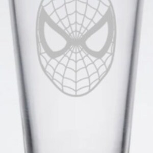 Puede incluir: Un vaso de pinta de vidrio transparente con un dise&ntilde;o grabado en blanco de la m&aacute;scara de Spider-Man.