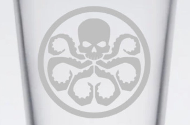 May include: A gray and white glass with a gray and white Hydra logo. The logo features a skull with a single eye and eight tentacles.