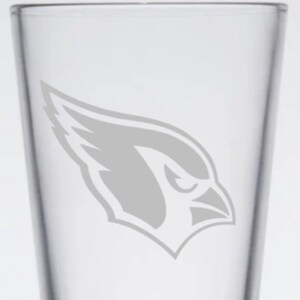 May include: A clear glass pint glass with a gray etched image of a cardinal bird's head with a wing on the side.