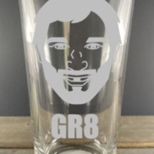 May include: A clear glass pint glass with a white silhouette of a man's face and the text "GR8" on the bottom.