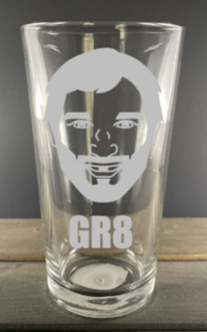 May include: A clear glass pint glass with a white silhouette of a man's face and the text "GR8" on the bottom.