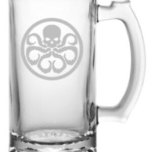 May include: A clear glass beer stein with a handle. The stein features an etched design of a skull with tentacles, a symbol often associated with the fictional organization HYDRA.