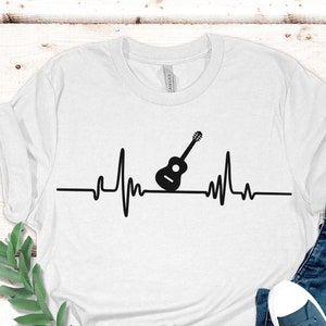 May include: White t-shirt with a black graphic of a guitar on a heartbeat line. The text "Shop Onlon" is on a circle with a leaf design.