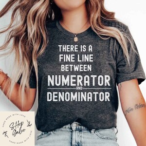 May include: A dark gray t-shirt with a white graphic that reads "There is a fine line between numerator and denominator".