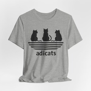 May include: A gray t-shirt with a black graphic of three cats sitting on a black and white striped design. The text "adicats" is below the cats.