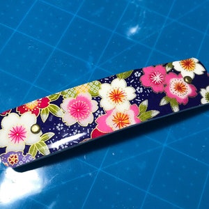 Handgefertigte französische Haarspange für mittleres bis dickes Haar. Misst 4,5x1. Mehrfarbige Kirschblüten auf blauem Hintergrund