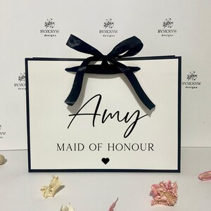 May include: White gift bag with a black ribbon and bow. The bag has black trim and the text "Amy Maid of Honour" printed on the front.