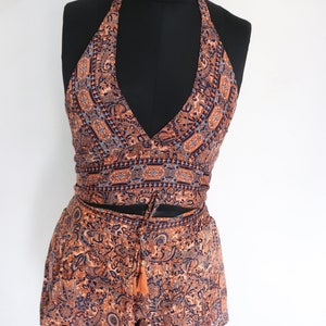May include: A two-piece halter top and shorts set. The set features a paisley pattern in shades of orange, navy blue, and grey. The top has a deep V-neck and a wrap-around design. The shorts have a drawstring waist.