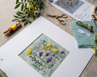 May include: An embroidery kit featuring a floral design with yellow and purple flowers, a snowflake, and a butterfly. The kit includes embroidery floss, fabric, a needle, scissors, and an embroidery hoop. The finished piece is displayed in a white mat.