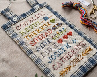 Puede incluir: Un sampler de punto de cruz con un borde de cuadros azules y blancos. El sampler presenta el texto "God Bless Kevin, Therese, Sydney, Alyse, Luna, Joseph & Catherine 2022".