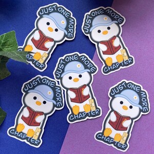Könnte beinhalten: Eine Sammlung von Aufklebern mit einem Cartoon-Pinguin mit blauer Mütze, der ein Buch liest. Die Aufkleber zeigen den Text "Just One More Chapter" und "Just One More". Der Pinguin trägt eine rote Weste.