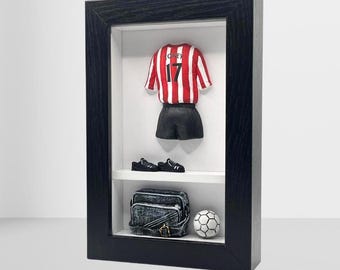 以下が含まれることがあります： 黒枠の影箱に、赤と白のサッカーユニフォーム（背番号17）、黒いショートパンツ、黒い靴、黒いバッグ、サッカーボールが入っています。