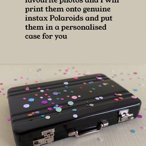 Op de afbeelding: Een zwarte, rechthoekige koffer met een zilveren handvat en een kleurrijk confetti-ontwerp. De koffer is gemaakt van metaal en heeft een sluiting aan de zijkant.