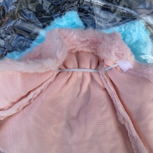 May include: A pink faux fur hooded sweater with a light blue lining. The sweater is made of a soft, knitted fabric.