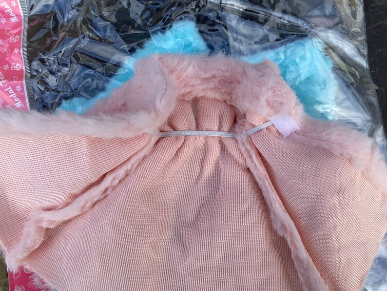 May include: A pink faux fur hooded sweater with a light blue lining. The sweater is made of a soft, knitted fabric.