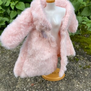 May include: A pink faux fur coat with a long sleeve and a collar. The coat is on a white mannequin.