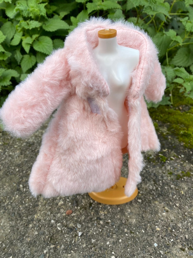 May include: A pink faux fur coat with a long sleeve and a collar. The coat is on a white mannequin.