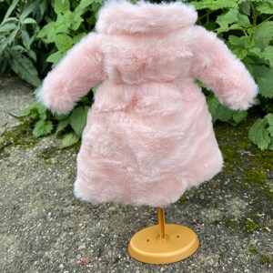 May include: A pink faux fur coat with a hood, displayed on a gold stand.