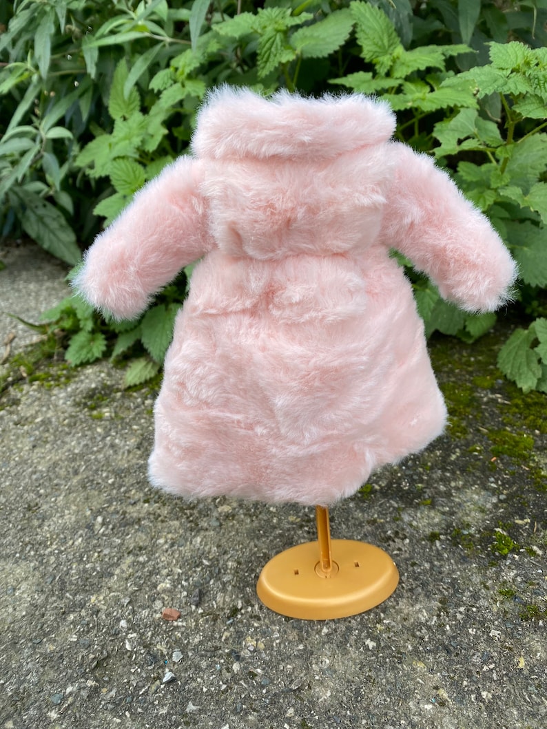 May include: A pink faux fur coat with a hood, displayed on a gold stand.
