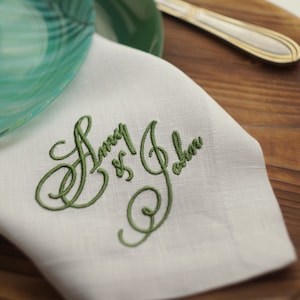 Può includere: Tovagliolo di lino bianco con ricamo verde che recita "Amy & John".
