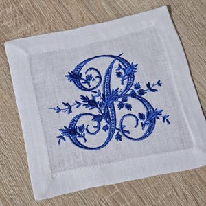 May include: A white linen napkin with a blue embroidered letter "B" surrounded by floral designs.