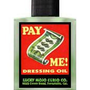 May include: A small green glass bottle with a black cap. The bottle has a red label with the words "PAY ME! DRESSING OIL" in white lettering. The label also features a green image of a rolled-up dollar bill with dollar signs printed on it. The bottle is labeled "LUCKY MOJO CURIO CO. 8223 Clover Road, Fontana, Cal."